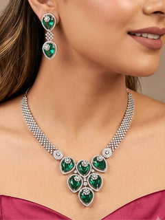 Close-up of a woman wearing an ornate Western (Silver Polish) Diamond Green Collar jewellery set and earrings with American Diamond and Green Colored Stones. Close-up shot of a high-quality American diamond artificial necklace worn for festive celebrations. Party wear outfit completed with a lightweight American diamond necklace.