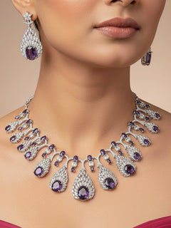Close-up of a woman wearing an ornate Western Purple Diamond Silver Collar jewellery set and earrings with American Diamond and Purple Colored Stones. A woman wearing a luxury American diamond necklace set styled beautifully for a wedding guest look in India. Elegant wedding jewelry look featuring a premium artificial American diamond necklace.