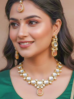 Close-up of a woman wearing an ornate traditional (Gold Polish) Peach Collar jewellery set and earrings and maangtikka with Kundan and American Diamonds. Woman wearing trending Kundan artificial jewelry for wedding season in India. Bride wearing a royal Kundan artificial necklace for wedding rituals.