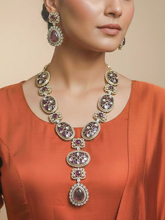 Close-up of a woman wearing an ornate traditional (Mehendi Gold Antique Finish) Purple long Colored Stone jewellery set and earrings with Kundan, Monalisa Stone and American Diamonds. Close-up of a premium imitation Colored Stones jewelry set styled with a aanarkali. Woman wearing trending Colored Stones artificial jewelry for wedding season in India.