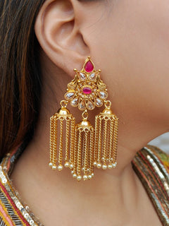 Close-up of a woman wearing Shivaya Earrings—elegant gold earrings adorned with ruby colored stones and Kundan, along with Three cascading chains ending in pearls. The intricate design is perfect for wedding ceremony jewelry.