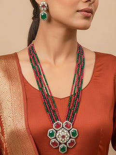 Close-up of a woman wearing an ornate traditional Diamond Ruby Red and Green jewellery set and earrings with Kundan, American Diamond, Monalisa Stones and Crystal Beads. A woman wearing a luxury American diamond necklace set styled beautifully for a wedding guest look in India. Elegant festive look with a high-quality imitation American diamond necklace set.
