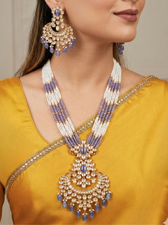 Close-up of a woman wearing an ornate traditional (Gold Polish) Lilac Long jewellery set and earrings with Polki, Tumble Beads, Crystal Beads, Pearls and Colored Stone. Woman styling a premium Polki imitation necklace for wedding celebrations. Wedding guest outfit styled with an elegant Polki necklace set.
