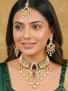 Close-up of a woman wearing an ornate traditional (Bright Gold) Red and Green Choker jewellery set and earrings and maangtikka with Uncut Kundan, American Diamond, Green Colored Stones, Pearls and Doublet Stone. Bride showcasing a premium imitation Moissanite jewelry set for her reception look. Wedding celebration styling with a luxury artificial Moissanite jewelry Set design.