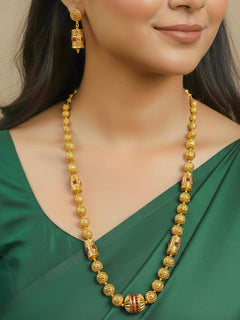 Close-up of a woman wearing an ornate traditional (Bright Gold Polish) Long Jewellery Set with Earrings with Ruby Red Colored Stones and Filigree Work. Saree look completed with an elegant Colored Stone artificial jewelry piece. Woman wearing trending Colored Stone artificial jewelry for wedding season in India.