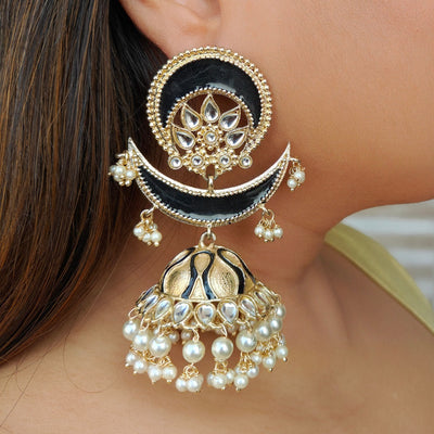 Close-up of a large, ornate gold earring with black accents, pearl beads, and intricate floral and crescent moon designs, worn by a person with long brown hair.