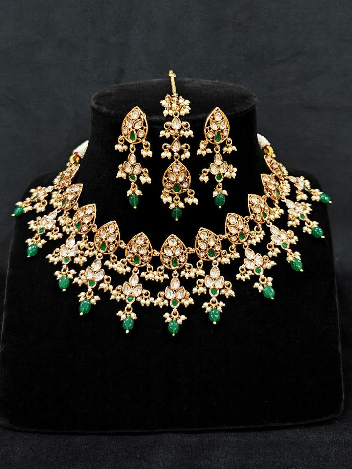 Close-up of an ornate traditional (Gold Polish) Green Collar jewellery set and earrings and maangtikka with Polki, Green Colored Stones, Tumble Beads and Pearls. Woman wearing trending Polki artificial jewelry for the wedding season in India. Woman wearing a lightweight Polki jewelry set for long wedding functions.