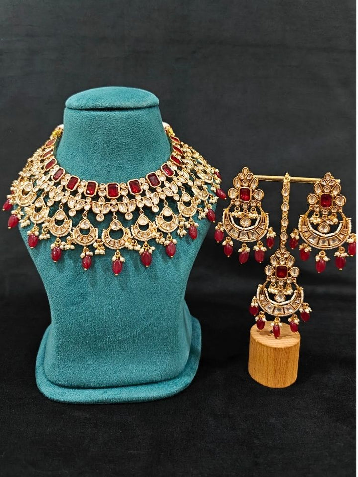 Close-up of an ornate traditional (Gold Polish) Collar jewellery set and earrings and maangtikka with Red Colored Stones, Polki, Kundan, Tumble beads and Pearls. Bride wearing a statement Polki jewelry set for wedding photos. Woman wearing trending Polki artificial jewelry for the wedding season in India.
