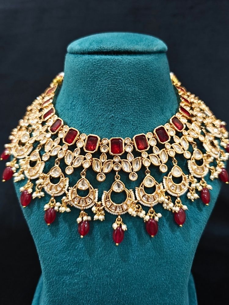 Close-up of an ornate traditional (Gold Polish) Collar jewellery set and earrings and maangtikka with Red Colored Stones, Polki, Kundan, Tumble beads and Pearls. Bride wearing a statement Polki jewelry set for wedding photos. Woman wearing trending Polki artificial jewelry for the wedding season in India.