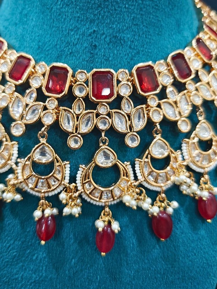 Close-up of an ornate traditional (Gold Polish) Collar jewellery set and earrings and maangtikka with Red Colored Stones, Polki, Kundan, Tumble beads and Pearls. Bride wearing a statement Polki jewelry set for wedding photos. Woman wearing trending Polki artificial jewelry for the wedding season in India.