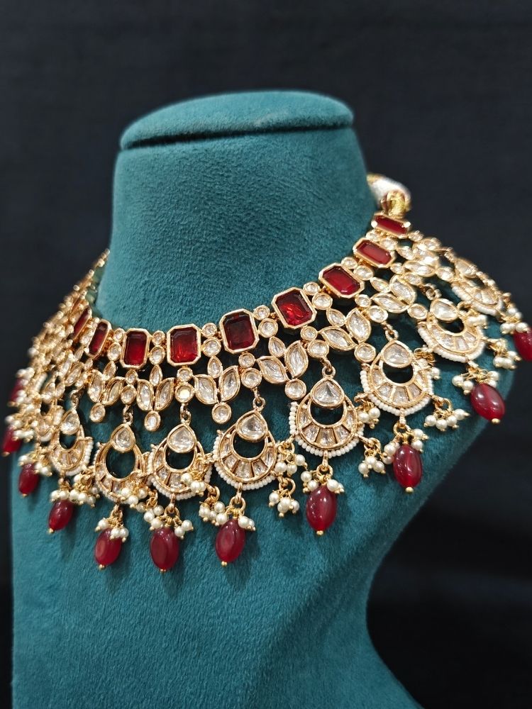 Close-up of an ornate traditional (Gold Polish) Collar jewellery set and earrings and maangtikka with Red Colored Stones, Polki, Kundan, Tumble beads and Pearls. Bride wearing a statement Polki jewelry set for wedding photos. Woman wearing trending Polki artificial jewelry for the wedding season in India.
