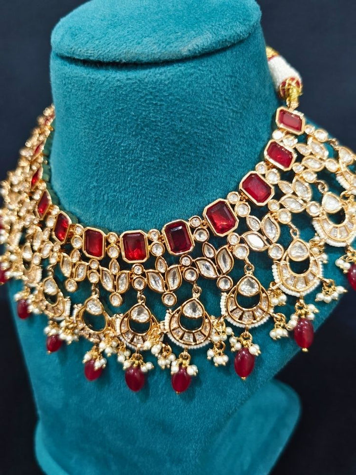 Close-up of an ornate traditional (Gold Polish) Collar jewellery set and earrings and maangtikka with Red Colored Stones, Polki, Kundan, Tumble beads and Pearls. Bride wearing a statement Polki jewelry set for wedding photos. Woman wearing trending Polki artificial jewelry for the wedding season in India.