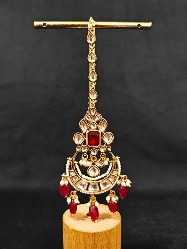 Close-up of an ornate traditional (Gold Polish) Collar jewellery set and earrings and maangtikka with Red Colored Stones, Polki, Kundan, Tumble beads and Pearls. Bride wearing a statement Polki jewelry set for wedding photos. Woman wearing trending Polki artificial jewelry for the wedding season in India.