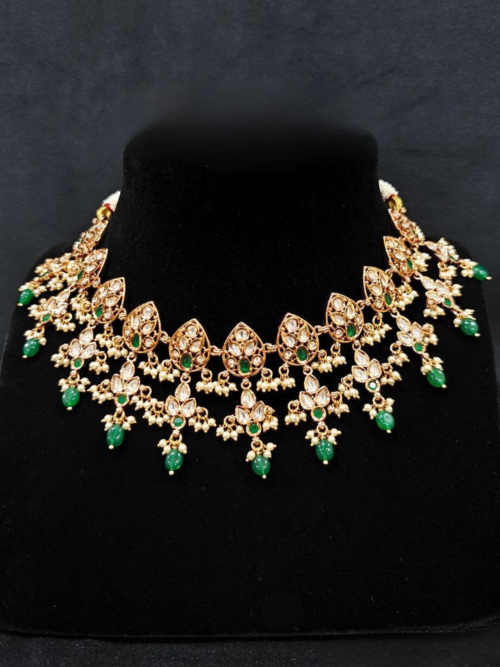 Close-up of a woman wearing an ornate traditional (Gold Polish) Green Collar jewellery set and earrings and maangtikka with Polki, Green Colored Stones, Tumble Beads and Pearls. Woman wearing trending Polki artificial jewelry for the wedding season in India. Woman wearing a lightweight Polki jewelry set for long wedding functions.