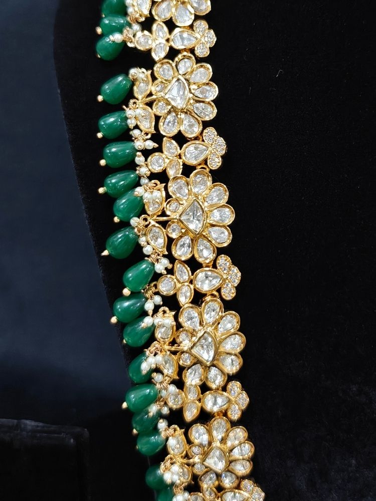 Close-up of an ornate traditional (Gold Polish) Long jewellery set and earrings with Polki, American Diamond Tumble Beads and Pearls. Wedding guest outfit styled with an elegant Polki necklace set. Woman Bridal mehendi outfit paired with a royal Polki artificial jewelry set. wearing trending Polki artificial jewelry for the wedding season in India. 