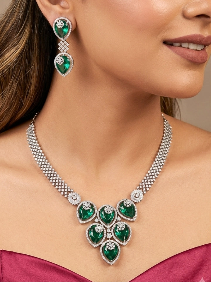 Close-up of a woman wearing an ornate Western (Silver Polish) Diamond Green Collar jewellery set and earrings with American Diamond and Green Colored Stones. Close-up shot of a high-quality American diamond artificial necklace worn for festive celebrations. Party wear outfit completed with a lightweight American diamond necklace.