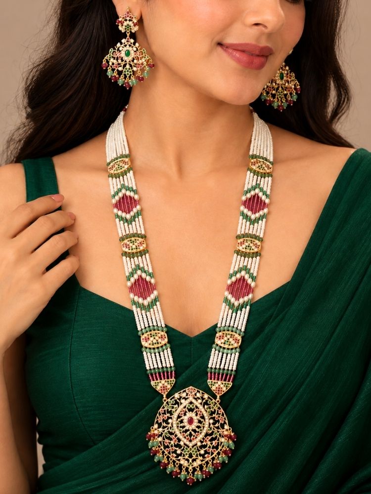 Suhana Jadau Necklace Set – woman wearing a long jadau necklace with ruby red, green and pearl bead strands and a jadau pendant and matching earrings, styled with a green outfit, artificial jewellery for weddings and bridal functions