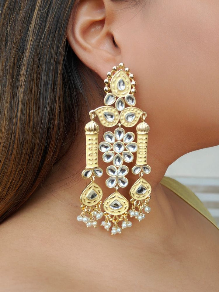 A close-up of a womans ear wearing Jasmine Yellow Earrings—large, ornate Meenakari long earrings with Yellow and gold accents, white kundan stones, pearl bead hangings, and intricate floral and geometric patterns.