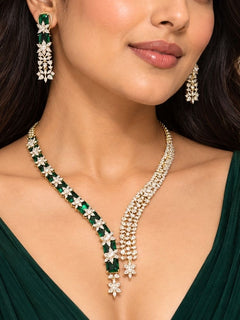 Electra Green Necklace Set – woman wearing a silver-tone American diamond necklace with emerald green stones and asymmetric drops and matching earrings, artificial jewellery for cocktail parties and engagement