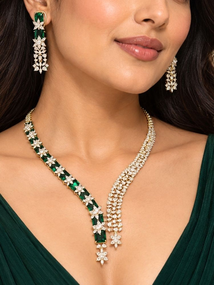 Electra Green Necklace Set – woman wearing a silver-tone American diamond necklace with emerald green stones and asymmetric drops and matching earrings, artificial jewellery for cocktail parties and engagement