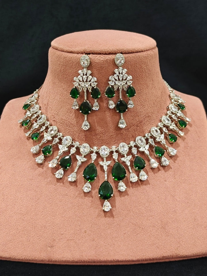 Close-up of an ornate Western (Silver Polish) Diamond Green Collar jewellery set and earrings with American Diamond and Green Colored Stone. Party wear outfit completed with a lightweight American diamond necklace. Elegant wedding jewelry look featuring a premium artificial American diamond necklace.