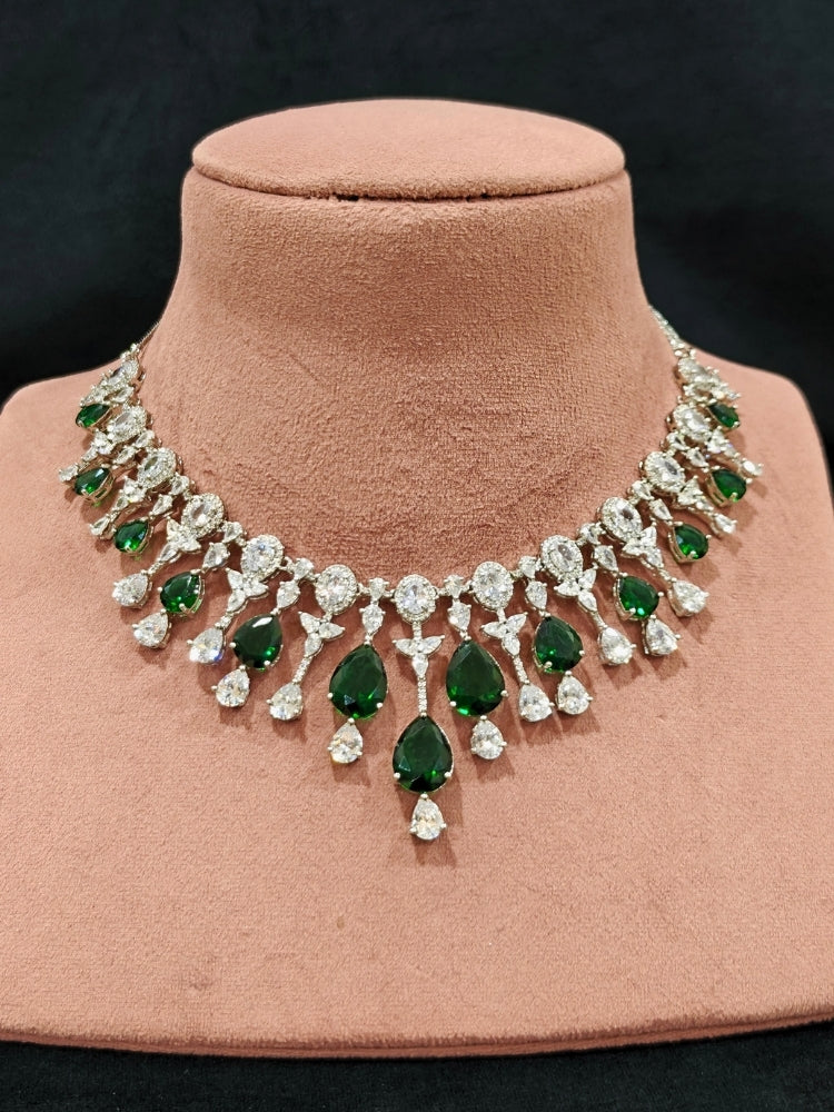 Close-up of an ornate Western (Silver Polish) Diamond Green Collar jewellery set and earrings with American Diamond and Green Colored Stone. Party wear outfit completed with a lightweight American diamond necklace. Elegant wedding jewelry look featuring a premium artificial American diamond necklace.