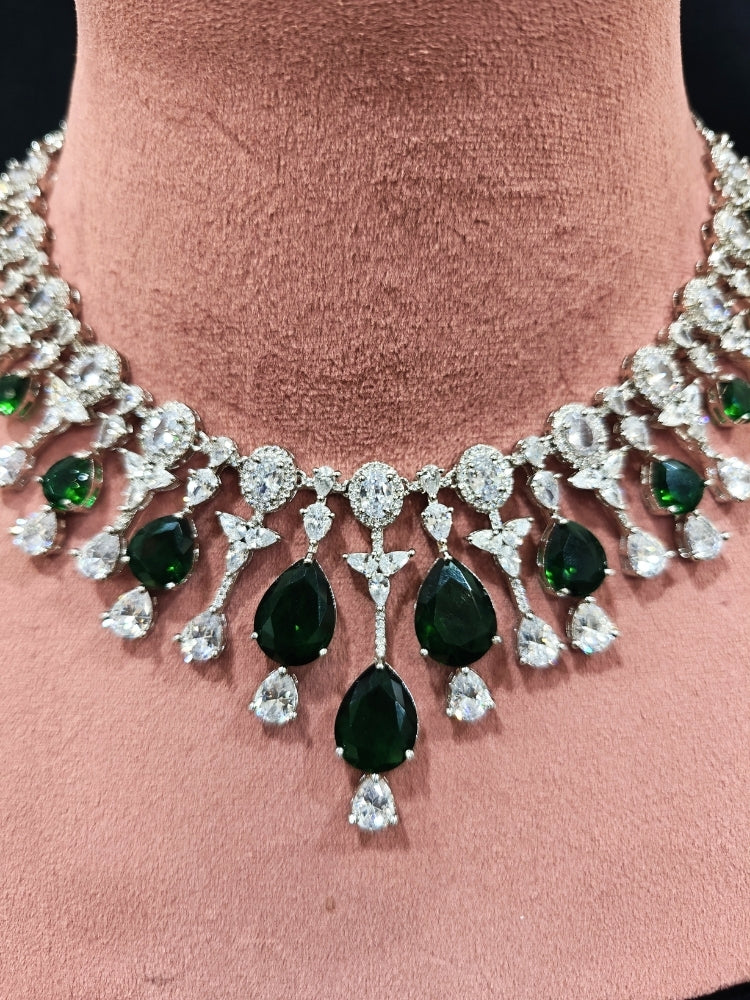 Close-up of an ornate Western (Silver Polish) Diamond Green Collar jewellery set and earrings with American Diamond and Green Colored Stone. Party wear outfit completed with a lightweight American diamond necklace. Elegant wedding jewelry look featuring a premium artificial American diamond necklace.