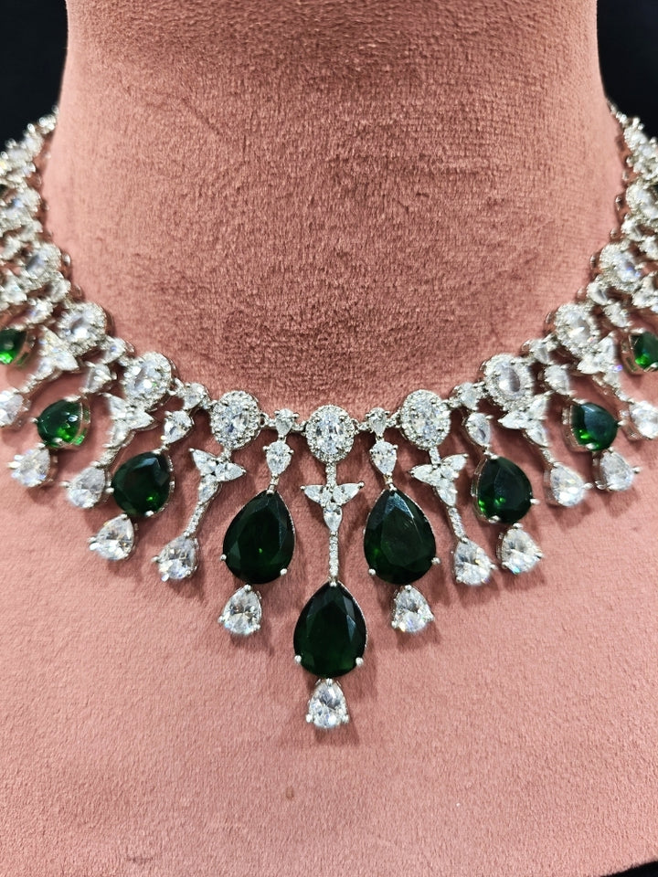Close-up of an ornate Western (Silver Polish) Diamond Green Collar jewellery set and earrings with American Diamond and Green Colored Stone. Party wear outfit completed with a lightweight American diamond necklace. Elegant wedding jewelry look featuring a premium artificial American diamond necklace.
