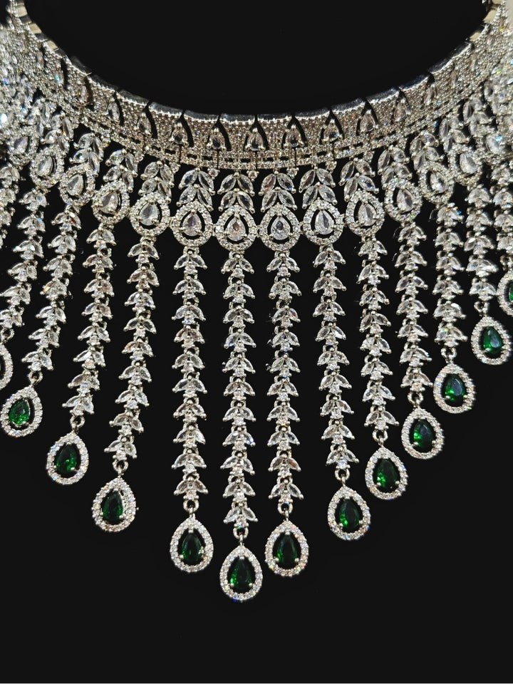 Close-up of an ornate Western (Silver Polish) Diamond Green Choker jewellery set and earrings with American Diamond and Green Colored Stones. Woman styling a statement American diamond necklace with an off-shoulder gown for a reception. A graceful woman wearing a trending American diamond necklace for a 2026 wedding celebration.