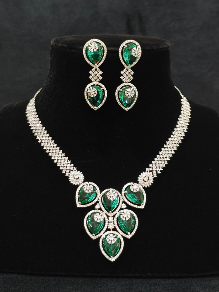 Close-up of an ornate Western (Silver Polish) Diamond Green Collar jewellery set and earrings with American Diamond and Green Colored Stones. Close-up shot of a high-quality American diamond artificial necklace worn for festive celebrations. Party wear outfit completed with a lightweight American diamond necklace.