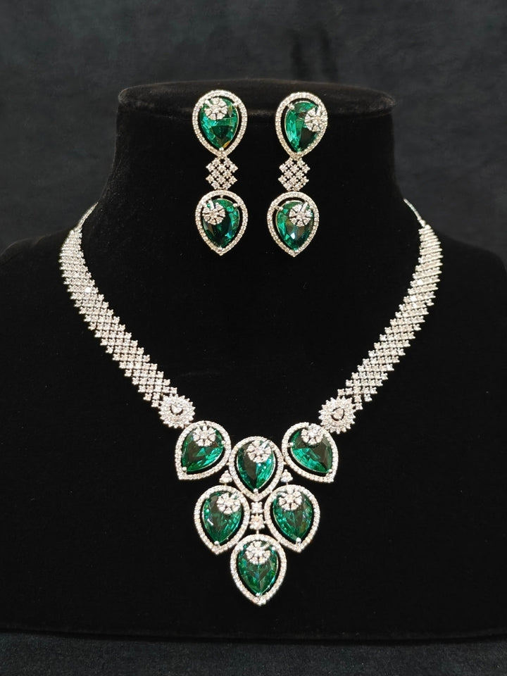 Close-up of an ornate Western (Silver Polish) Diamond Green Collar jewellery set and earrings with American Diamond and Green Colored Stones. Close-up shot of a high-quality American diamond artificial necklace worn for festive celebrations. Party wear outfit completed with a lightweight American diamond necklace.