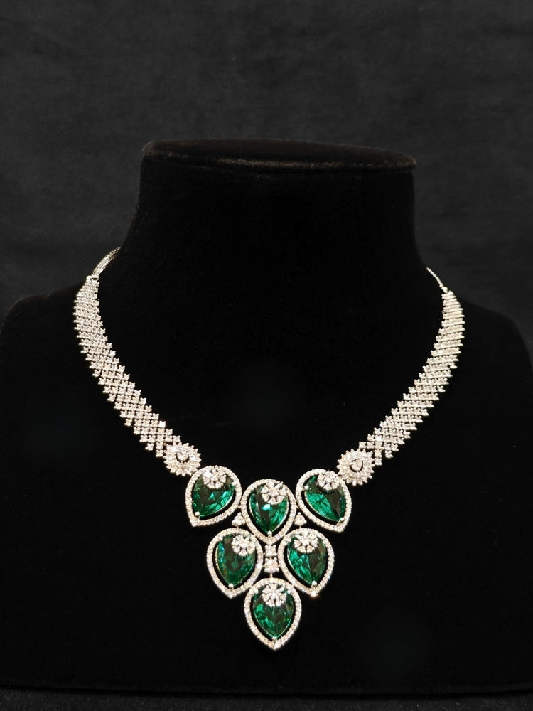 Close-up of an ornate Western (Silver Polish) Diamond Green Collar jewellery set and earrings with American Diamond and Green Colored Stones. Close-up shot of a high-quality American diamond artificial necklace worn for festive celebrations. Party wear outfit completed with a lightweight American diamond necklace.