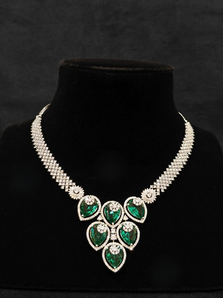 Close-up of an ornate Western (Silver Polish) Diamond Green Collar jewellery set and earrings with American Diamond and Green Colored Stones. Close-up shot of a high-quality American diamond artificial necklace worn for festive celebrations. Party wear outfit completed with a lightweight American diamond necklace.
