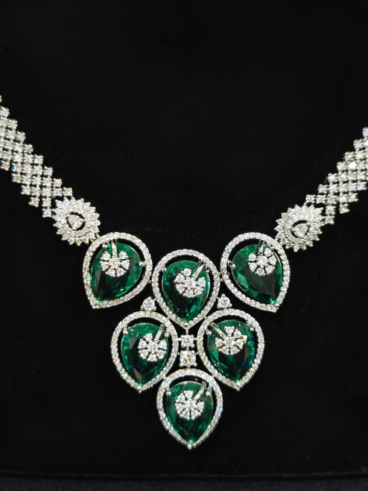 Close-up of an ornate Western (Silver Polish) Diamond Green Collar jewellery set and earrings with American Diamond and Green Colored Stones. Close-up shot of a high-quality American diamond artificial necklace worn for festive celebrations. Party wear outfit completed with a lightweight American diamond necklace.