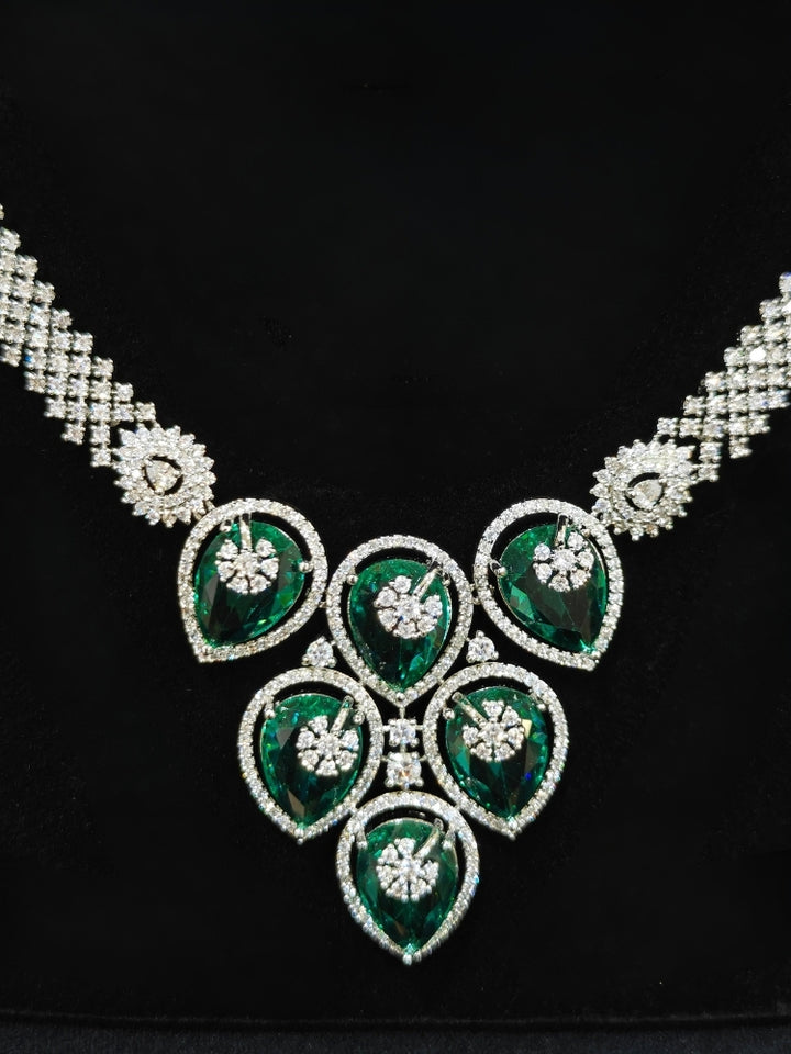 Close-up of an ornate Western (Silver Polish) Diamond Green Collar jewellery set and earrings with American Diamond and Green Colored Stones. Close-up shot of a high-quality American diamond artificial necklace worn for festive celebrations. Party wear outfit completed with a lightweight American diamond necklace.