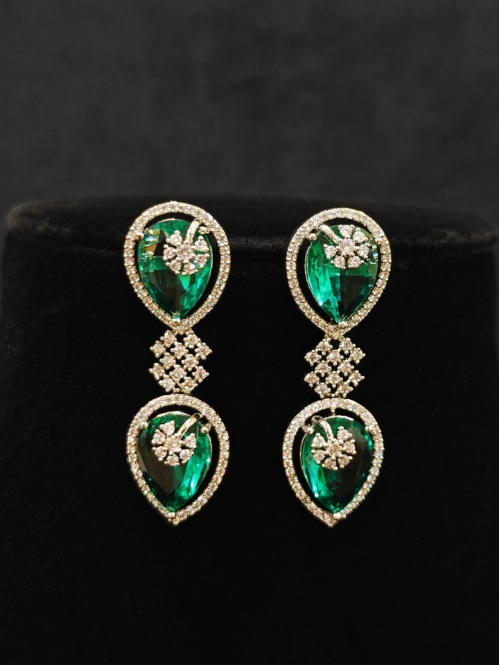 Close-up of an ornate Western (Silver Polish) Diamond Green Collar jewellery set and earrings with American Diamond and Green Colored Stones. Close-up shot of a high-quality American diamond artificial necklace worn for festive celebrations. Party wear outfit completed with a lightweight American diamond necklace.