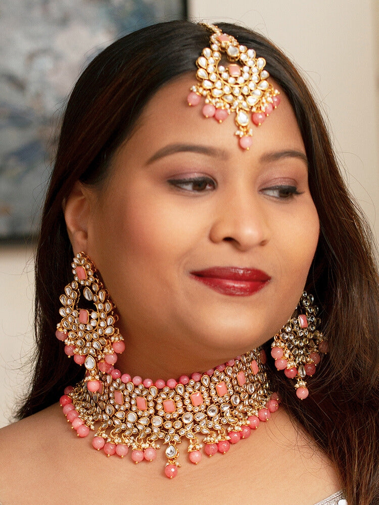 Close-up of a woman wearing an ornate traditional Pink Kundan Choker jewellery set and earrings and maangtikka with Kundan, Mint Pink Stone, Pearls and Mint Pink Crystal Beads. Bride wearing a royal Kundan artificial necklace for wedding rituals. Wedding celebration look enhanced with a statement Kundan necklace. 