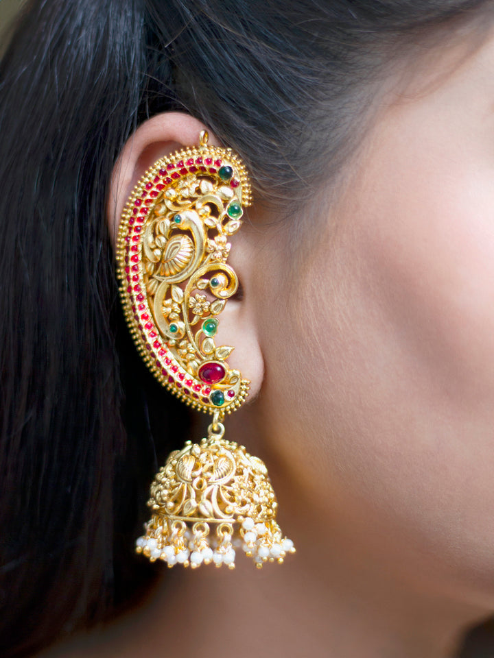 A close-up of a womans ear adorned with Aarzoo Kaanphool Earrings—ornate gold earrings featuring colorful gemstones, intricate designs, and pearl-accented hanging jhumka—ideal as ethnic or wedding jewelry. The earring covers her entire ear giving an exclusive look. 