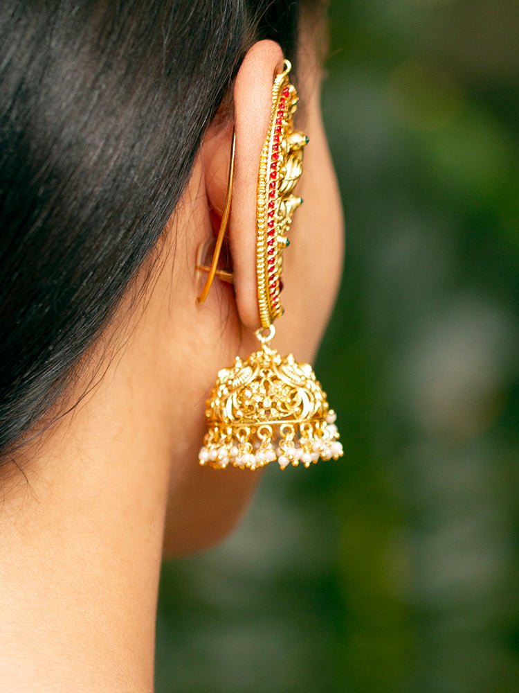 A close-up of a womans ear adorned with Aarzoo Kaanphool Earrings—ornate gold earrings featuring colorful gemstones, intricate designs, and pearl-accented hanging jhumka—ideal as ethnic or wedding jewelry. The earring covers her entire ear giving an exclusive look. 