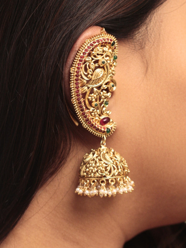 A close-up of a womans ear adorned with Aarzoo Kaanphool Earrings—ornate gold earrings featuring colorful gemstones, intricate designs, and pearl-accented hanging jhumka—ideal as ethnic or wedding jewelry. The earring covers her entire ear giving an exclusive look. 