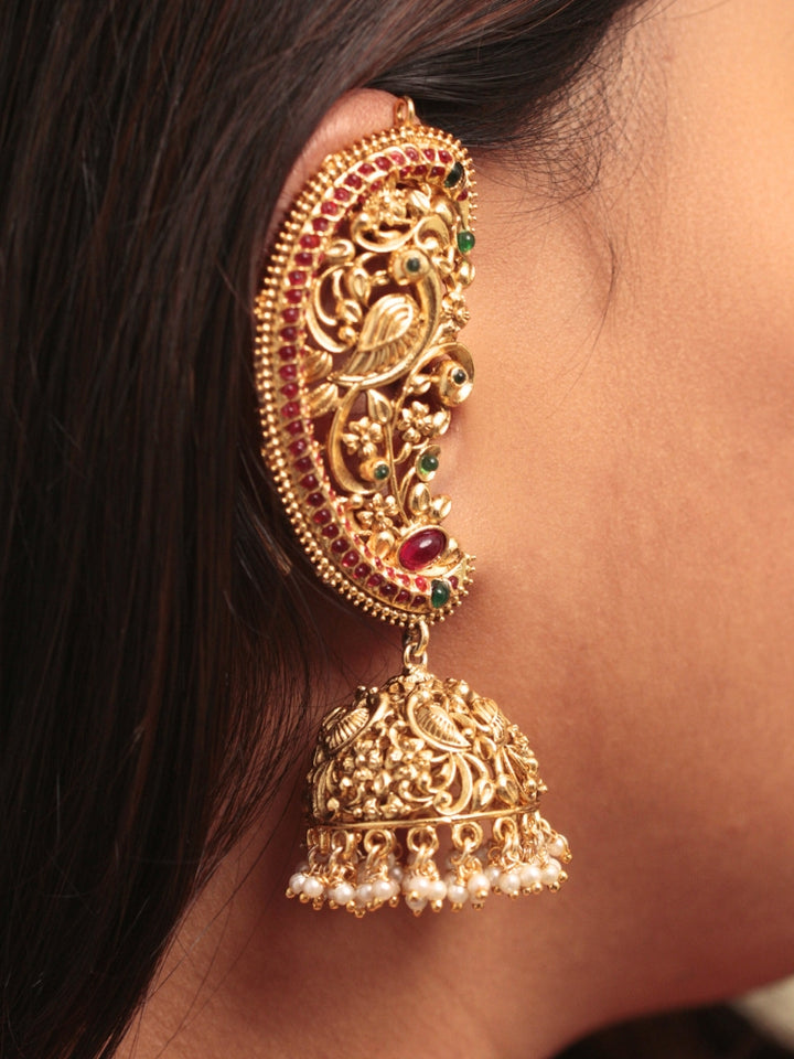 A close-up of a womans ear adorned with Aarzoo Kaanphool Earrings—ornate gold earrings featuring colorful gemstones, intricate designs, and pearl-accented hanging jhumka—ideal as ethnic or wedding jewelry. The earring covers her entire ear giving an exclusive look. 