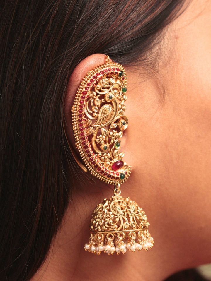 A close-up of a womans ear adorned with Aarzoo Kaanphool Earrings—ornate gold earrings featuring colorful gemstones, intricate designs, and pearl-accented hanging jhumka—ideal as ethnic or wedding jewelry. The earring covers her entire ear giving an exclusive look. 