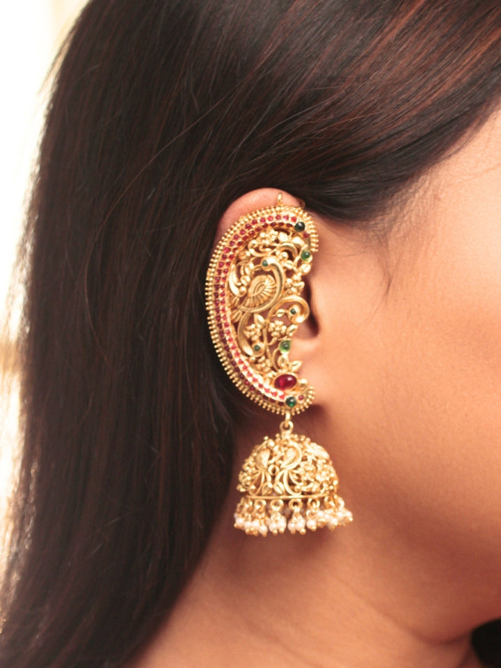 A close-up of a womans ear adorned with Aarzoo Kaanphool Earrings—ornate gold earrings featuring colorful gemstones, intricate designs, and pearl-accented hanging jhumka—ideal as ethnic or wedding jewelry. The earring covers her entire ear giving an exclusive look. 