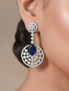 Close-up of a woman wearing an ornate Western (Silver Polish) Blue Diamond Earrings with American Diamond and Colored Stones. Bride wearing luxury artificial American Diamond earrings for reception night. Reception-ready look completed with statement artificial jewelry American Diamond earrings.