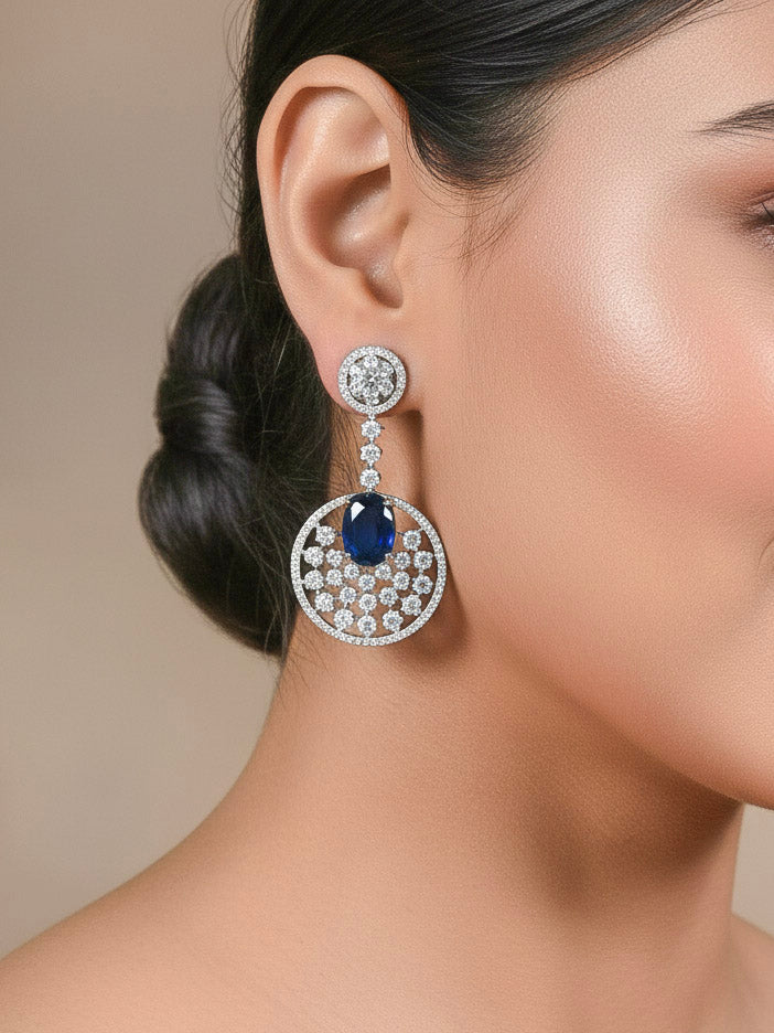 Close-up of a woman wearing an ornate Western (Silver Polish) Blue Diamond Earrings with American Diamond and Colored Stones. Bride wearing luxury artificial American Diamond earrings for reception night. Reception-ready look completed with statement artificial jewelry American Diamond earrings.