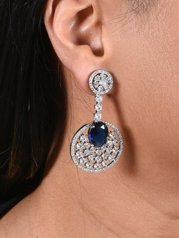 Close-up of a woman wearing an ornate Western (Silver Polish) Blue Diamond Earrings with American Diamond and Colored Stones. Bride wearing luxury artificial American Diamond earrings for reception night. Reception-ready look completed with statement artificial jewelry American Diamond earrings.