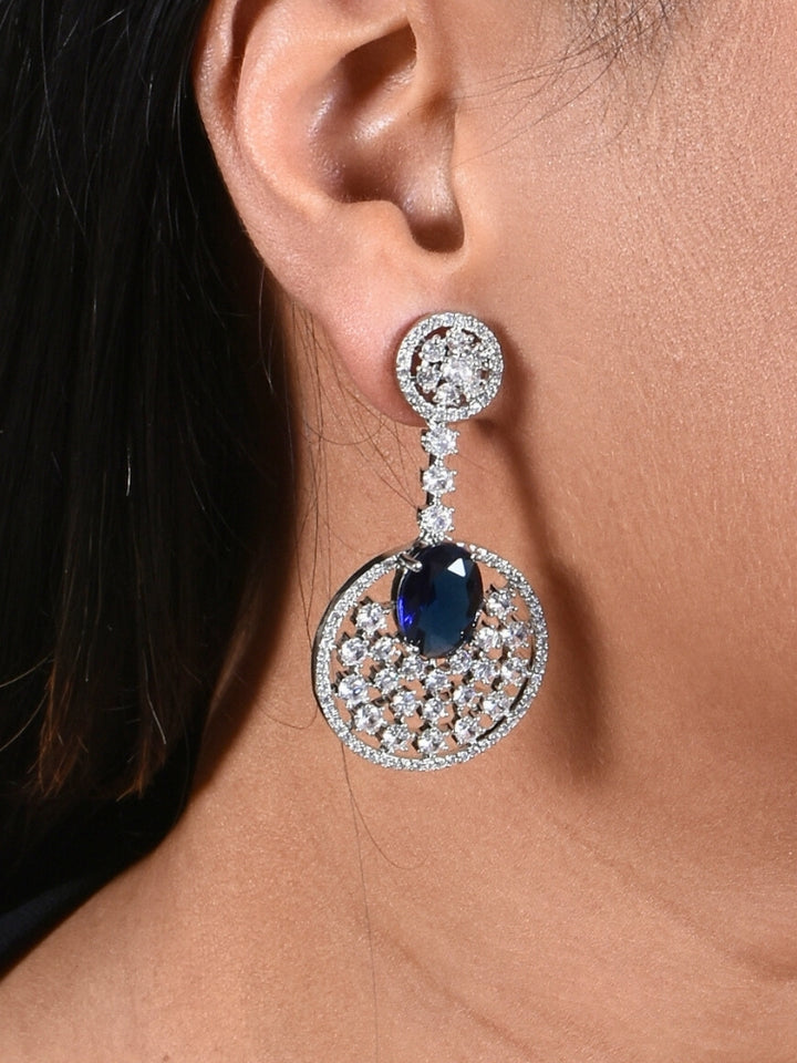 Close-up of a woman wearing an ornate Western (Silver Polish) Blue Diamond Earrings with American Diamond and Colored Stones. Bride wearing luxury artificial American Diamond earrings for reception night. Reception-ready look completed with statement artificial jewelry American Diamond earrings.