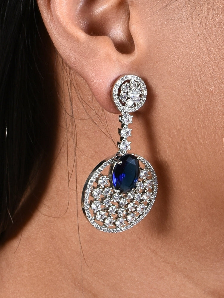 Close-up of a woman wearing an ornate Western (Silver Polish) Blue Diamond Earrings with American Diamond and Colored Stones. Bride wearing luxury artificial American Diamond earrings for reception night. Reception-ready look completed with statement artificial jewelry American Diamond earrings.