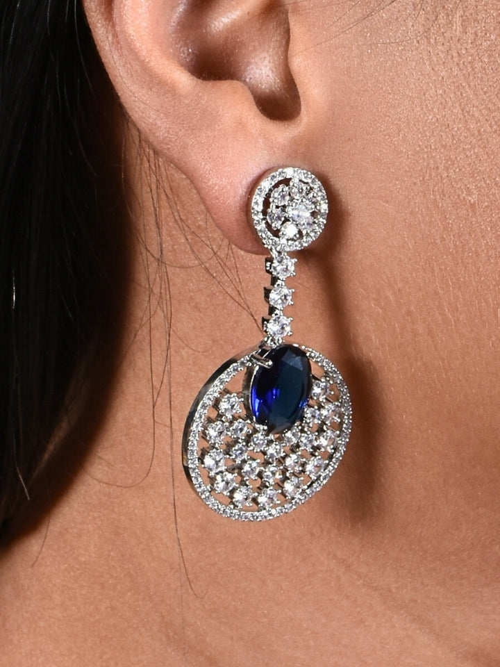 Close-up of a woman wearing an ornate Western (Silver Polish) Blue Diamond Earrings with American Diamond and Colored Stones. Bride wearing luxury artificial American Diamond earrings for reception night. Reception-ready look completed with statement artificial jewelry American Diamond earrings.