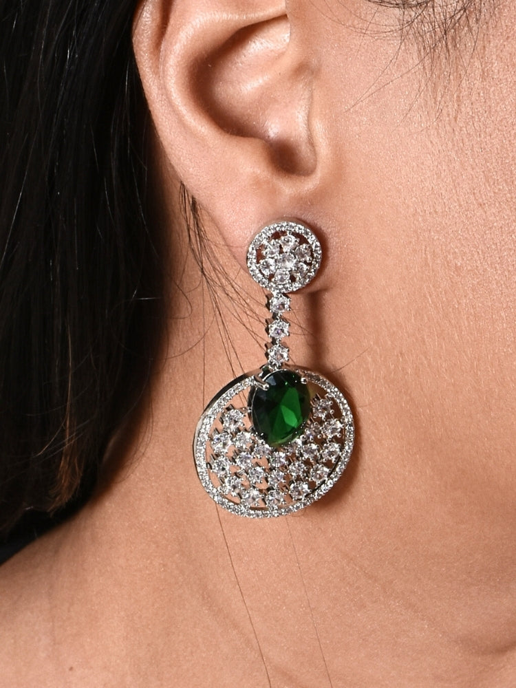 Close-up of a woman wearing an ornate Western (Silver Polish) Green Diamond Earrings with American Diamond and Colored Stones. Bride wearing luxury artificial American Diamond earrings for reception night. Reception-ready look completed with statement artificial jewelry American Diamond earrings.